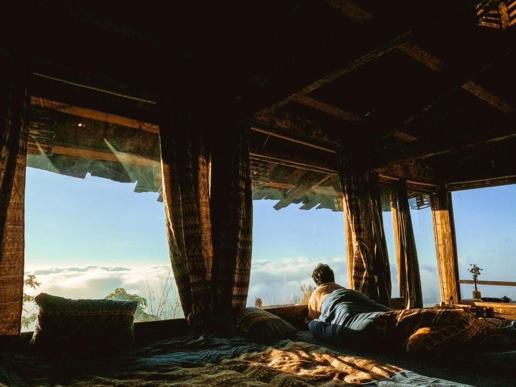 a man laying on a bed looking out of a window at 1941M Homestay Tà Xùa in Bắc Yên