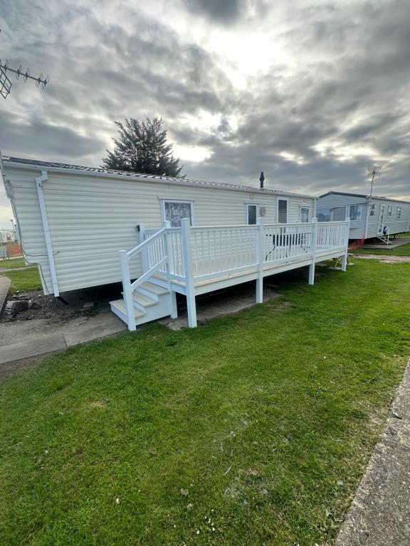 a white mobile home with a porch and a yard at Angie's caravan at Seawick in Saint Osyth