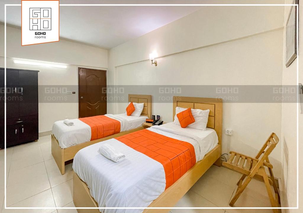 Un dormitorio con 2 camas y una silla. en GOHO Rooms 10th Commercial en Karachi