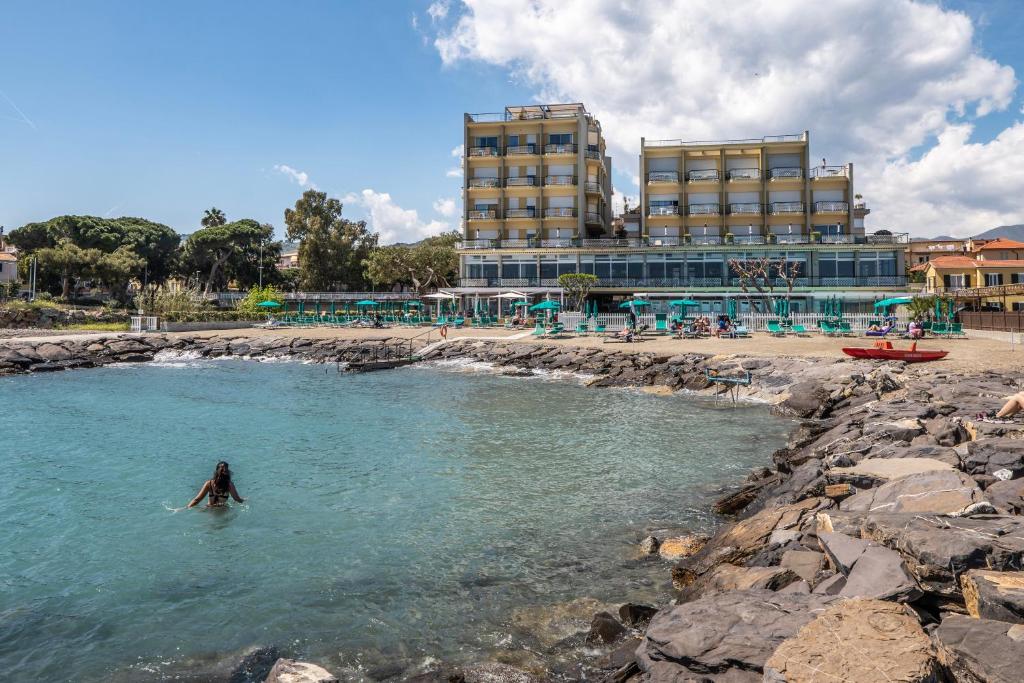 una persona in acqua vicino a una spiaggia con un edificio di Hotel Bellevue Et Mediterranée a Diano Marina