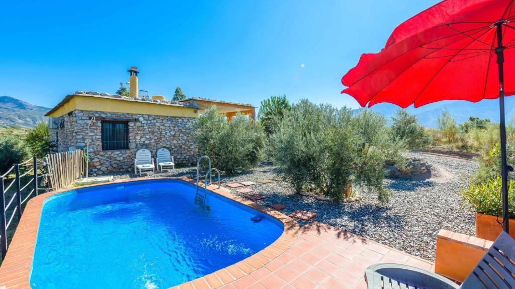 une maison avec une piscine et un parasol rouge dans l'établissement El Secano de Paco Órgiva by Ruralidays, à Órgiva