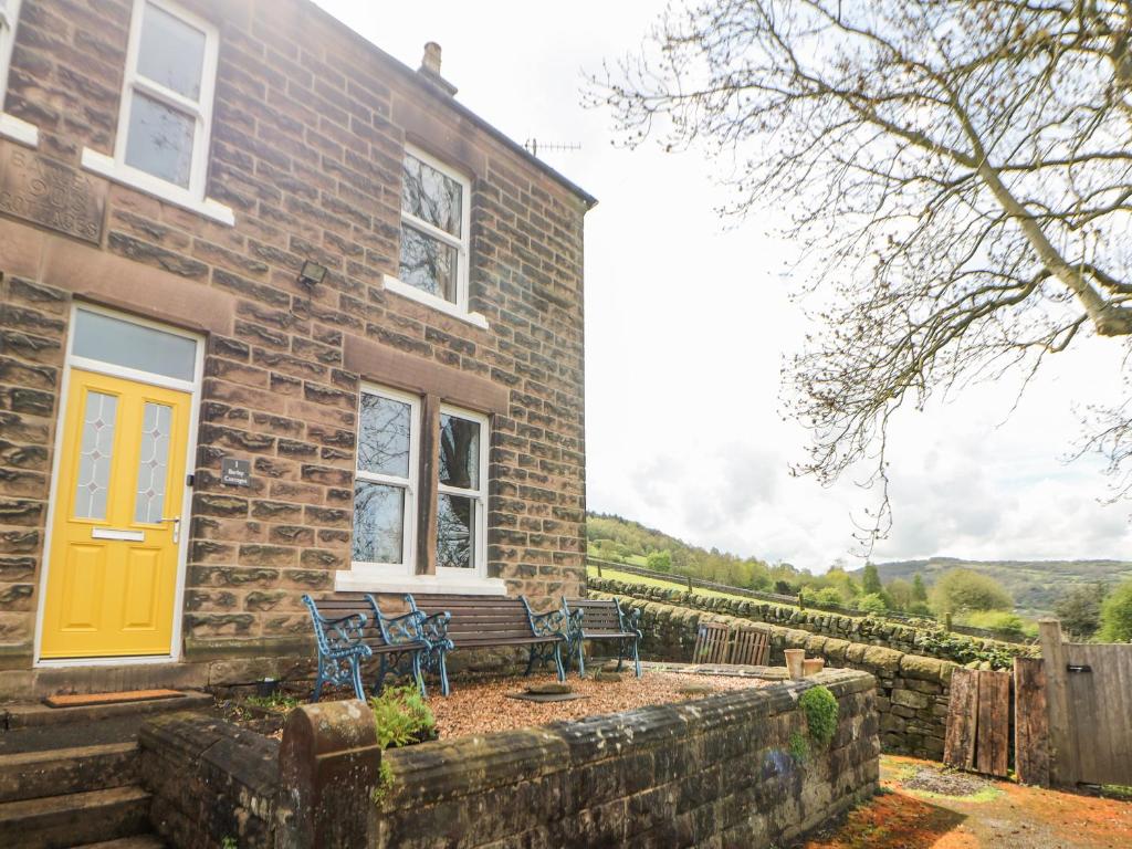 a brick house with a yellow door and a bench at 1 Barley Cottages in Matlock