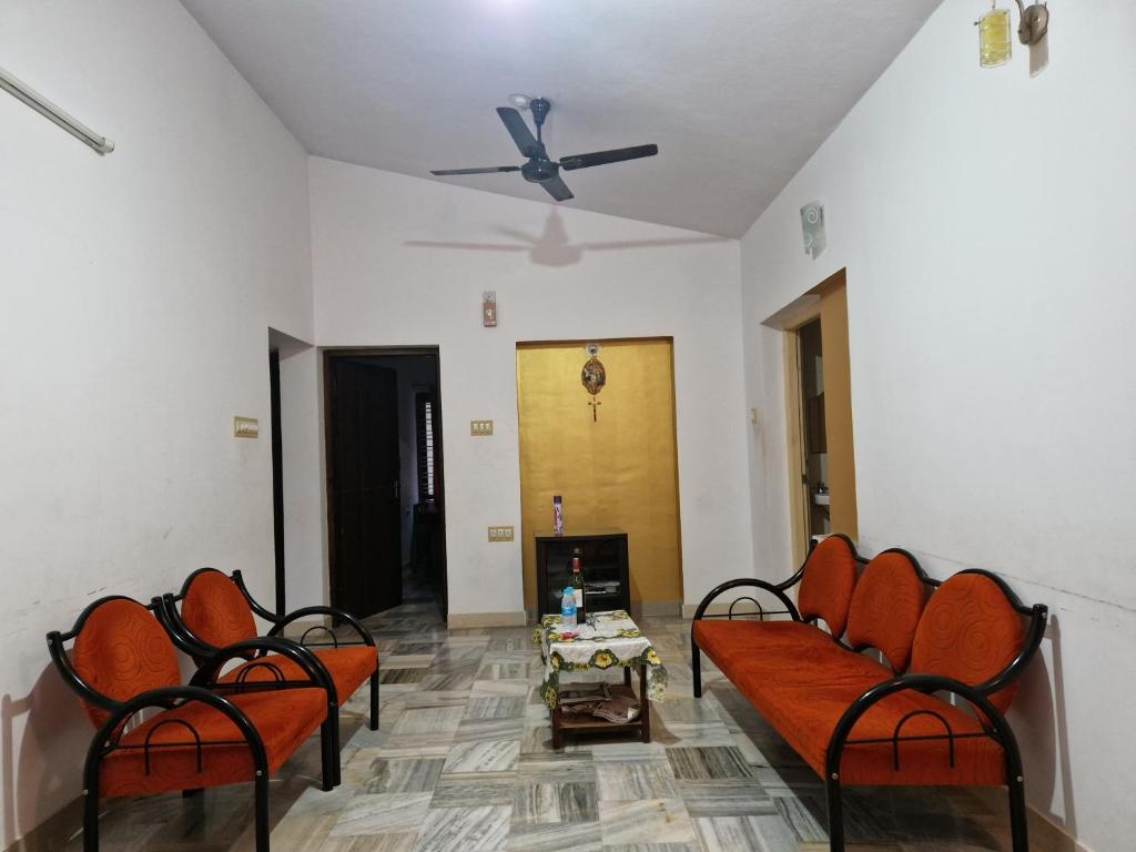 a living room with orange chairs and a ceiling fan at Gladsvilla in Mangalore