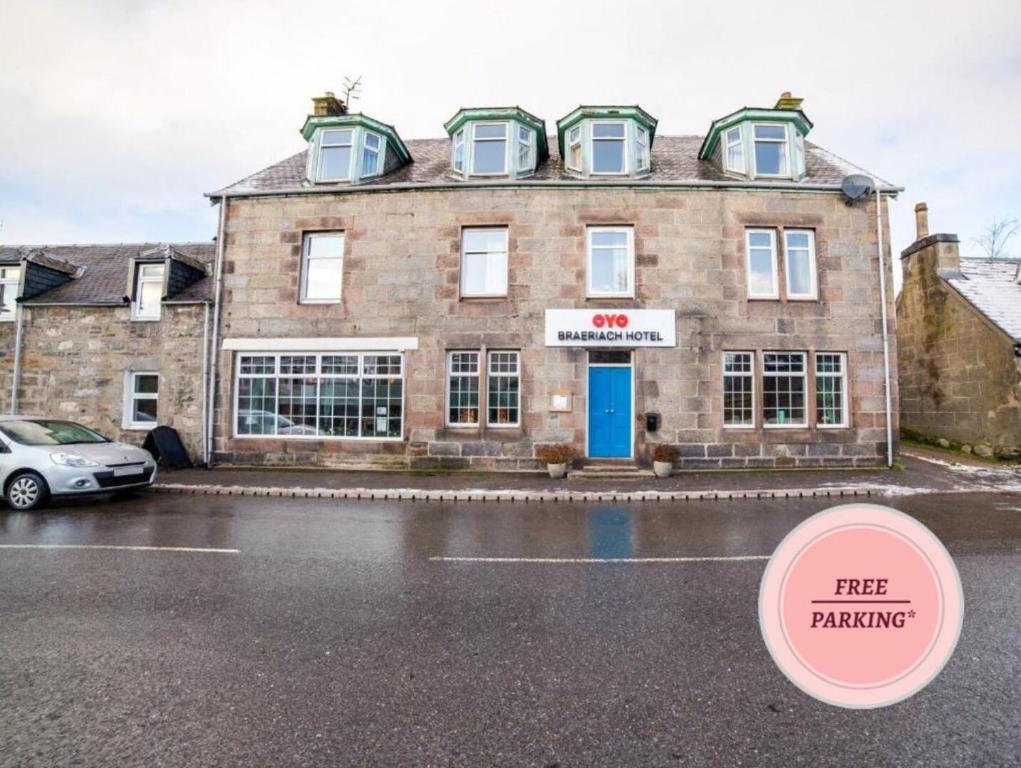 un antiguo edificio de ladrillo con una señal de aparcamiento gratuita delante de él en OYO Braeriach Hotel, Highlands Scotland en Newtonmore