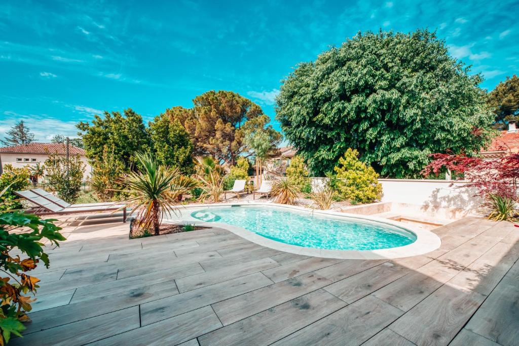 a swimming pool in a backyard with a wooden deck and a tree at Villa luxe Oasis de Satteva in L&#39;Isle-sur-la-Sorgue