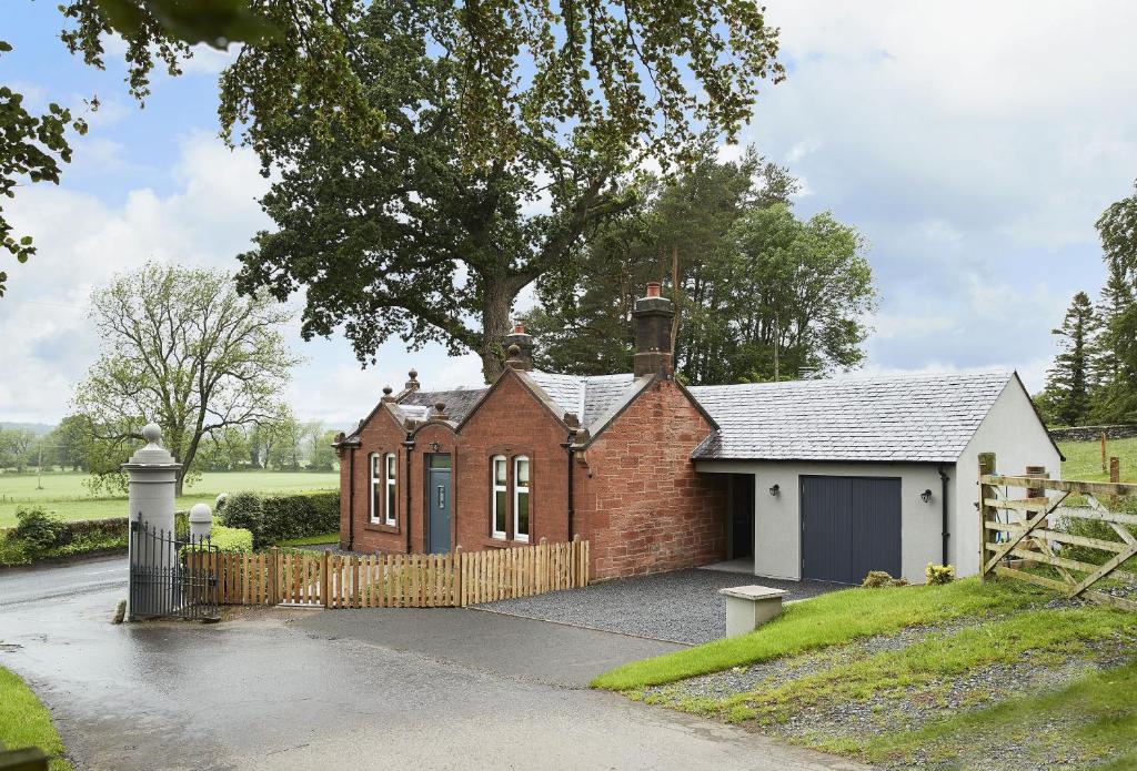 a small brick house with a fence and a tree at Netherwood Lodge in Dumfries