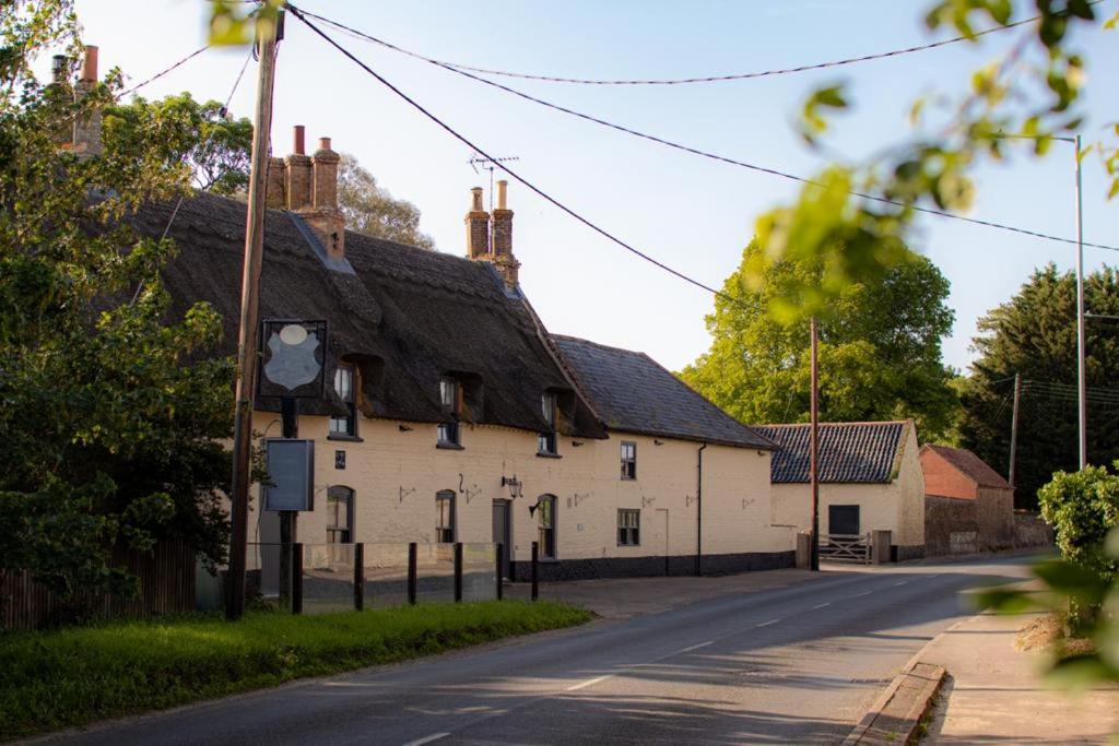 a white building with a black roof on a street at Breckland Thatched Cottage in Hockwold cum Wilton