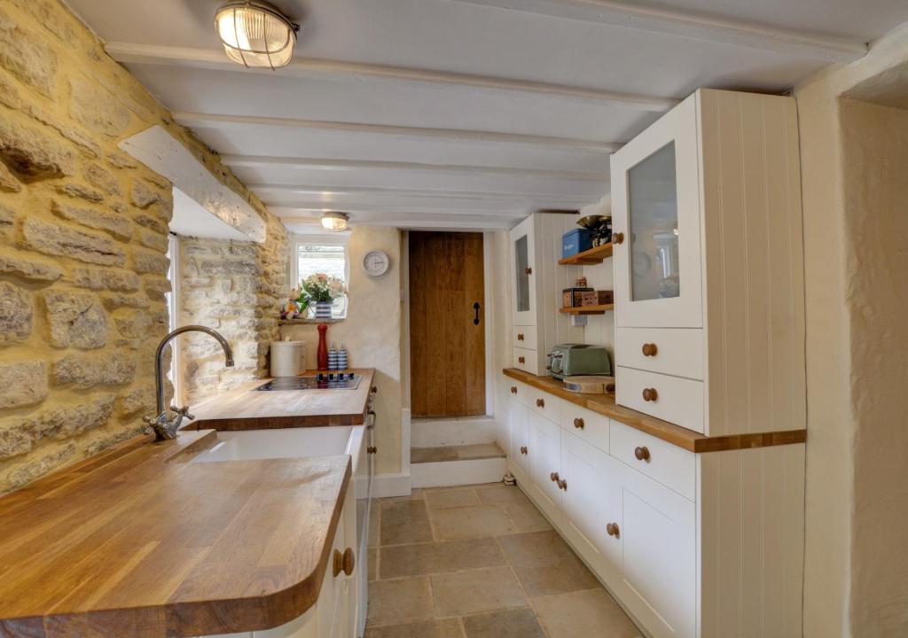 a kitchen with white cabinets and a stone wall at Little Steppes in Swanage