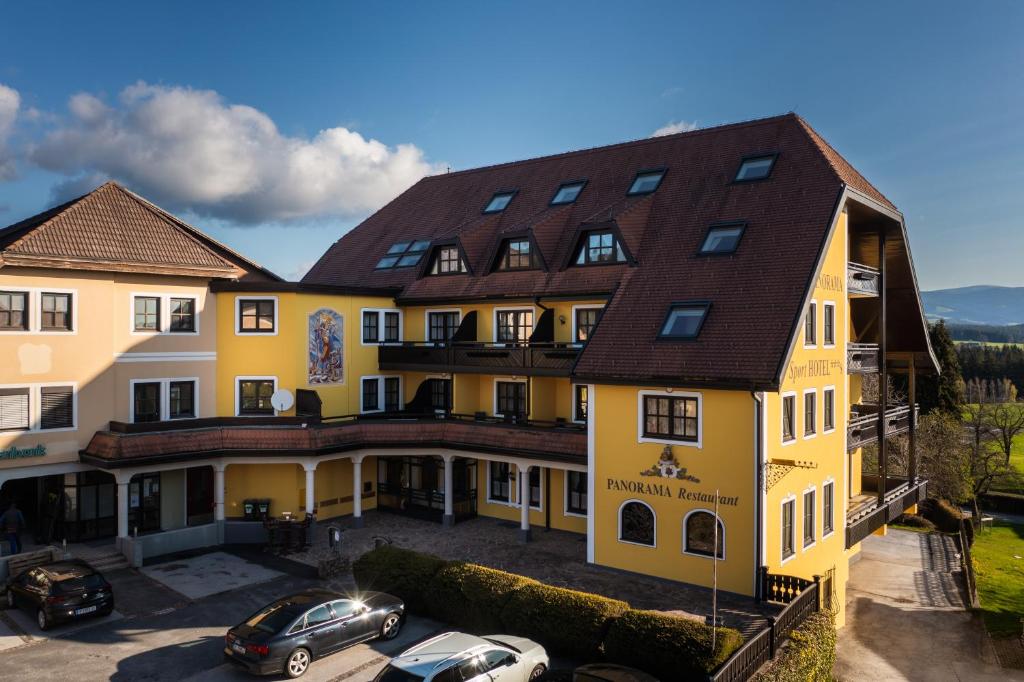 een groot geel gebouw met auto's geparkeerd op een parkeerplaats bij PANORAMA SportHOTEL in Wenigzell