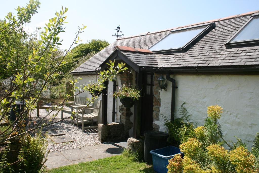 a small white cottage with a solar roof at Cosy barn on rural smallholding with alpacas, goats & pigs in Stithians