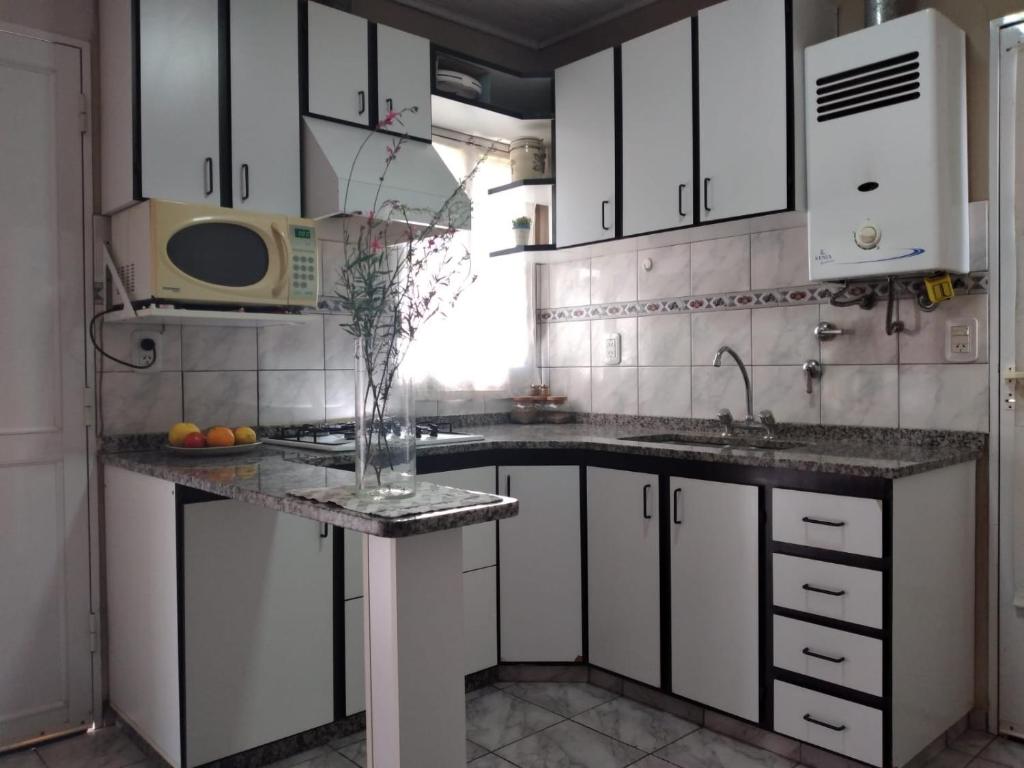 a kitchen with white cabinets and a vase of flowers on a counter at Alojamiento Turístico Los Pinos in Villa Elisa