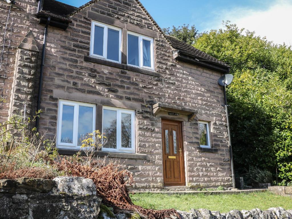 a stone cottage with a wooden door and windows at Wayland House in Bakewell