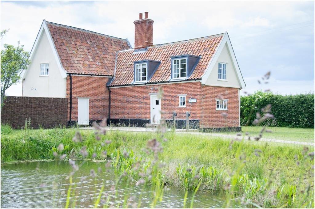 an old brick house next to a body of water at The Cottage, High Ash Farm in Peasenhall