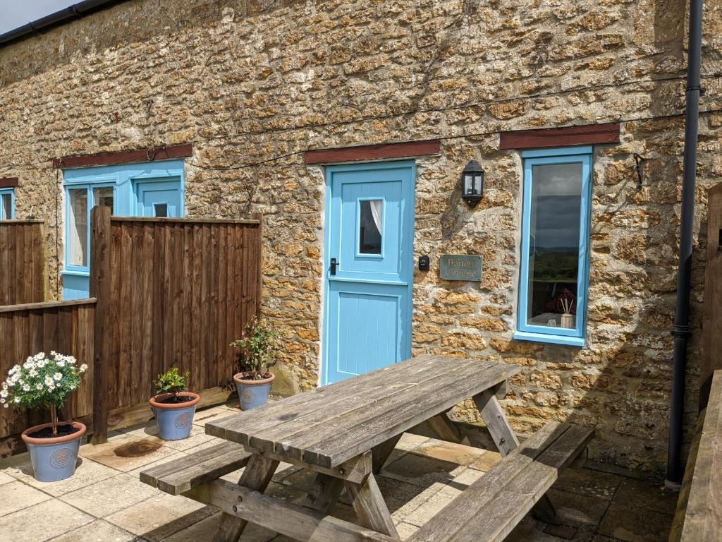 een houten picknicktafel voor een stenen gebouw met een blauwe deur bij Barton Cottage in Bridport