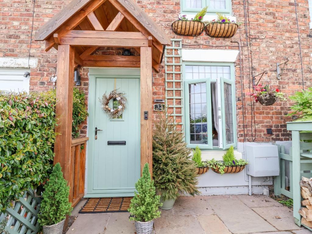 a brick house with a blue door and potted plants at Wisteria Cottage in Nantwich