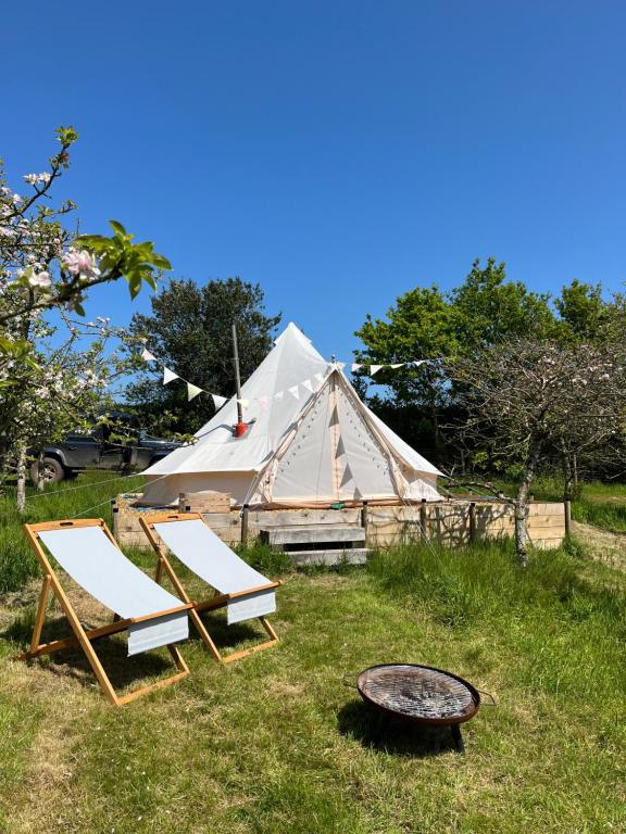 a tent with two chairs and a grill in the grass at Bowhayes Farm - Camping and Glamping in Venn Ottery