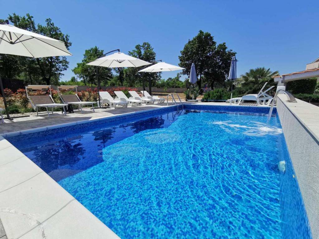 a blue swimming pool with chairs and umbrellas at Apartments Lea with pool in Malinska