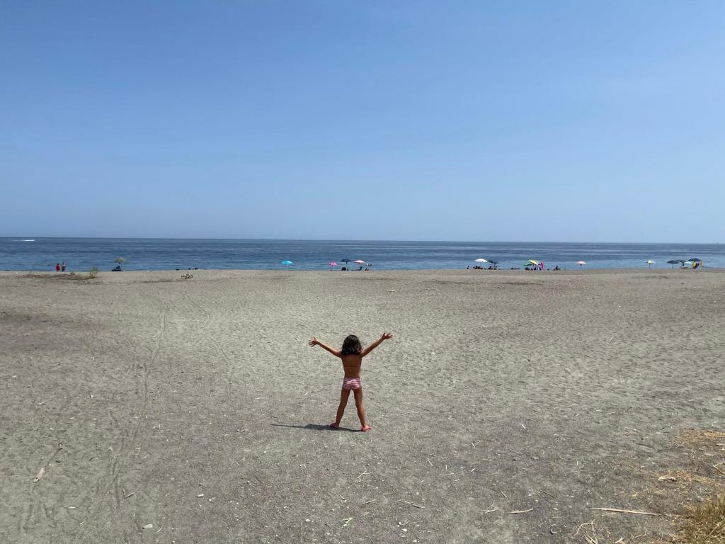 a girl standing on a beach with her arms outstretched at Serena Holiday Home Calatabiano in Calatabiano