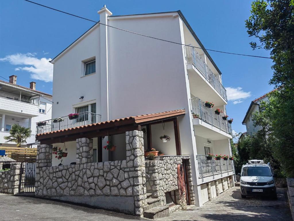 ein weißes Gebäude mit einer Steinmauer neben einem Auto in der Unterkunft Apartments Iva in Crikvenica