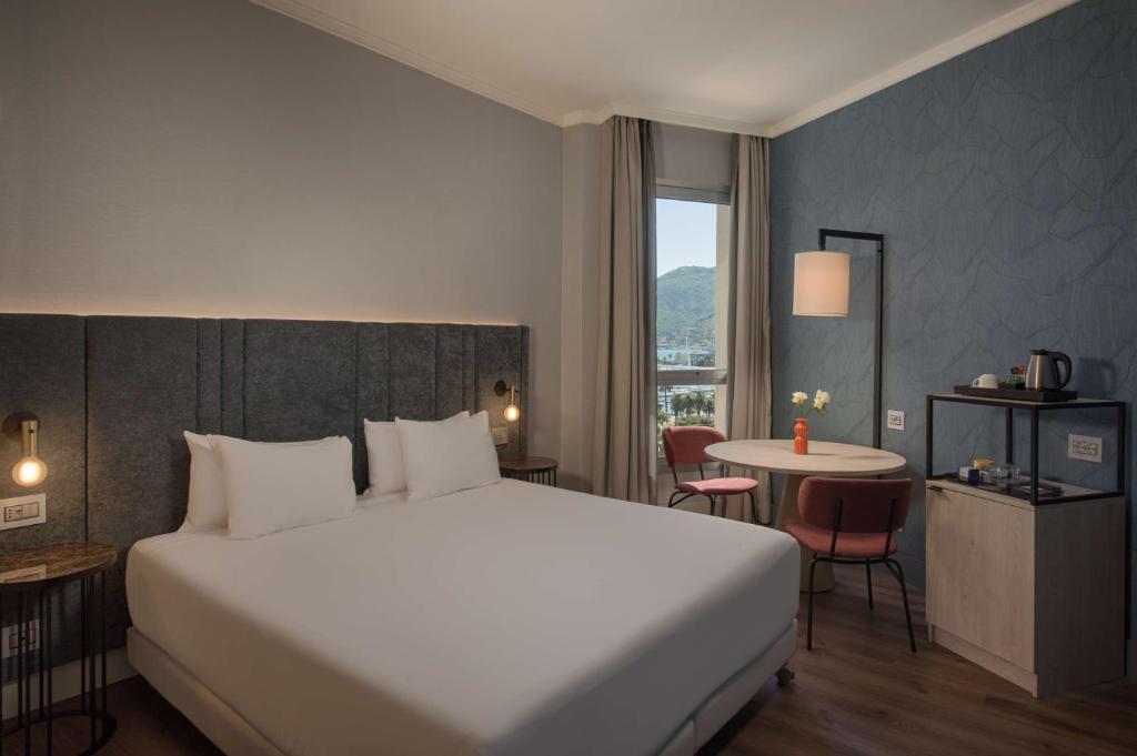 ein Hotelzimmer mit einem großen Bett und einem Tisch in der Unterkunft NH La Spezia in La Spezia