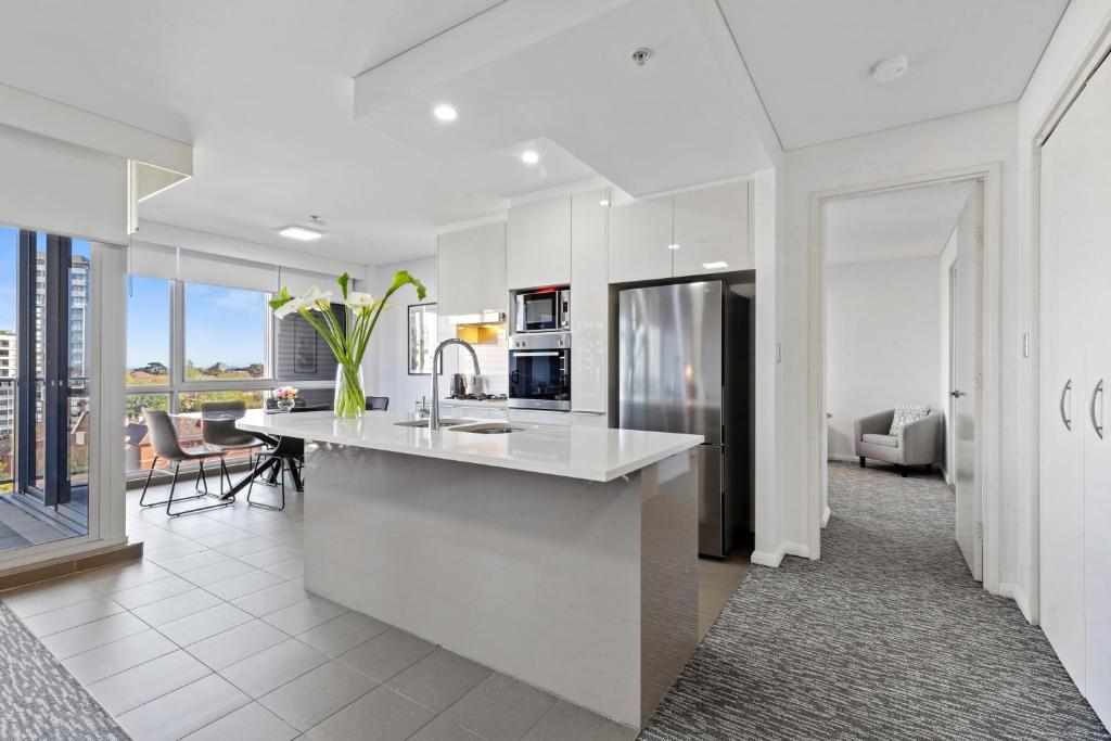 a white kitchen with a counter and a living room at AAN Apartments North Sydney in Sydney