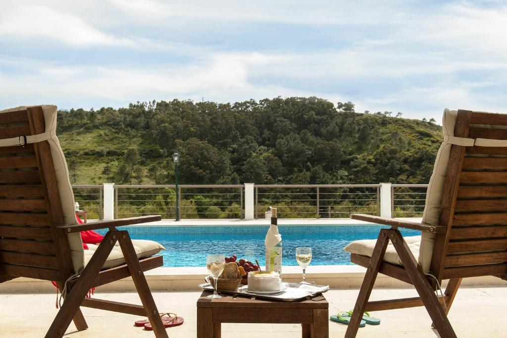 埃里塞拉的住宿－Beachouse - Surf, Bed & Breakfast，游泳池畔的两把椅子和一张桌子及一瓶葡萄酒