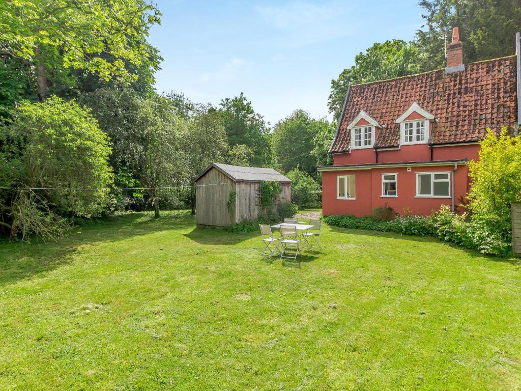 un patio con una casa roja, una mesa y sillas en Oaklawn Cottage, en Eye