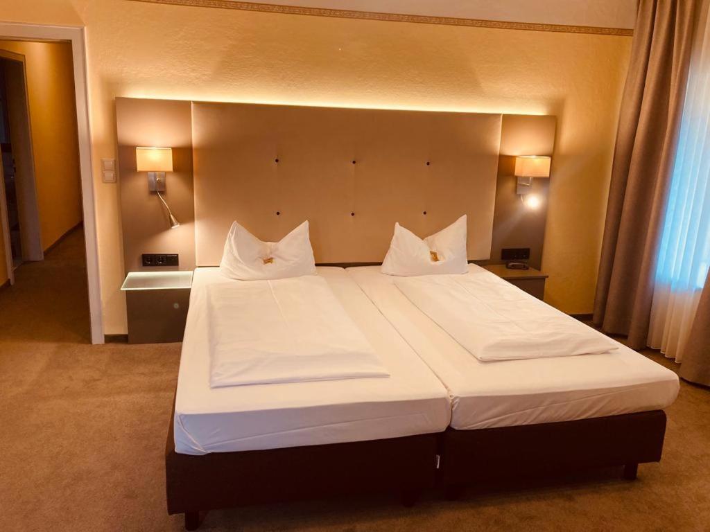 um quarto com uma cama grande com lençóis brancos e almofadas em Hotel Rosenheimer Hof em Traunstein