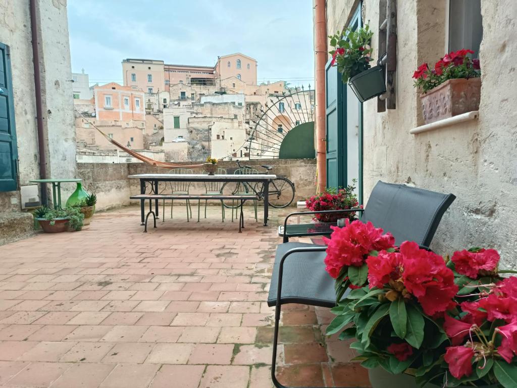 un patio con mesas, sillas y flores rojas en Spartivento Apartments en Matera