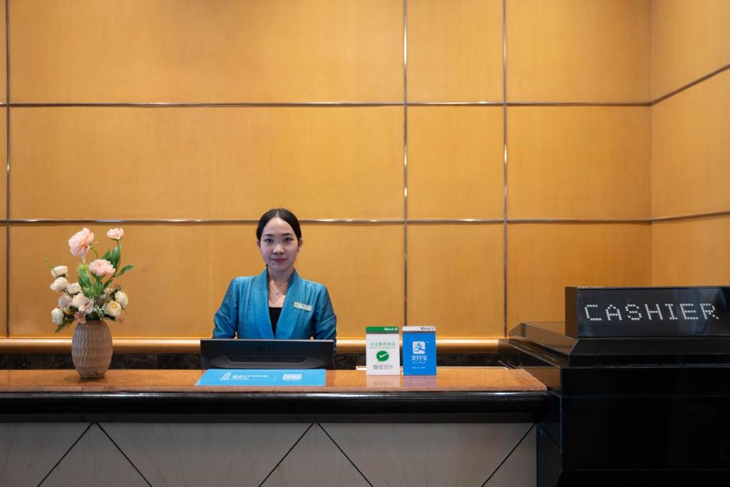 A front-desk staff member sits behind a polished cashier counter in a wood-paneled reception area.