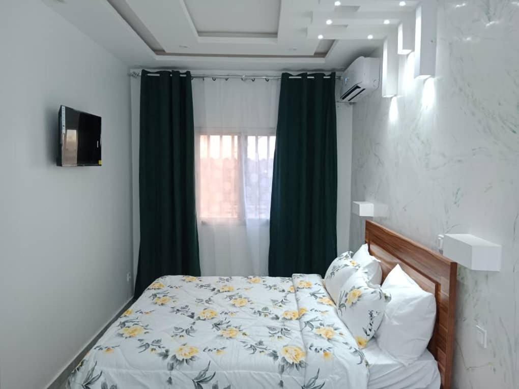 een slaapkamer met een bed en een raam met groene gordijnen bij Studio Emeraude - cosy et climatisé - Résidence Saraba Mermoz in Dakar