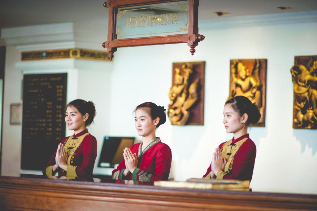Three uniformed staff members stand behind the hotel reception counter.
