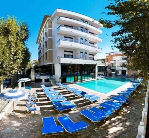 a swimming pool with blue lounge chairs and a building at Hotel Queen Mary in Cattolica