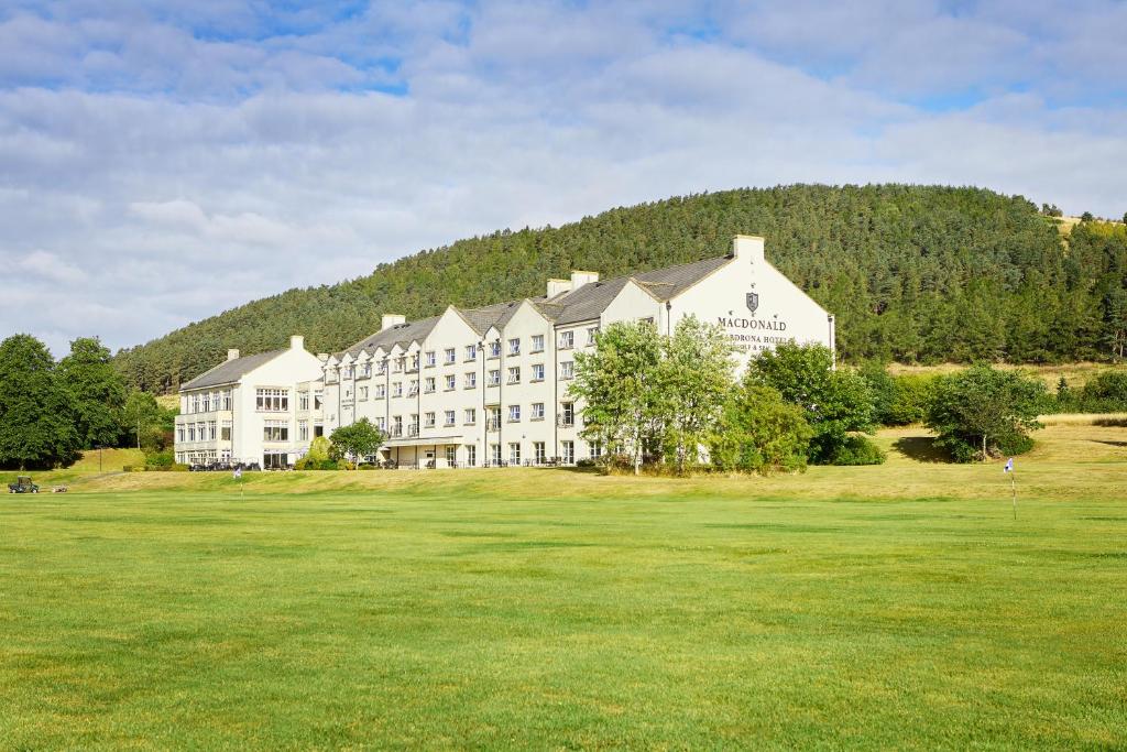 a large white building on top of a green field at Macdonald Cardrona Hotel, Golf & Spa in Peebles