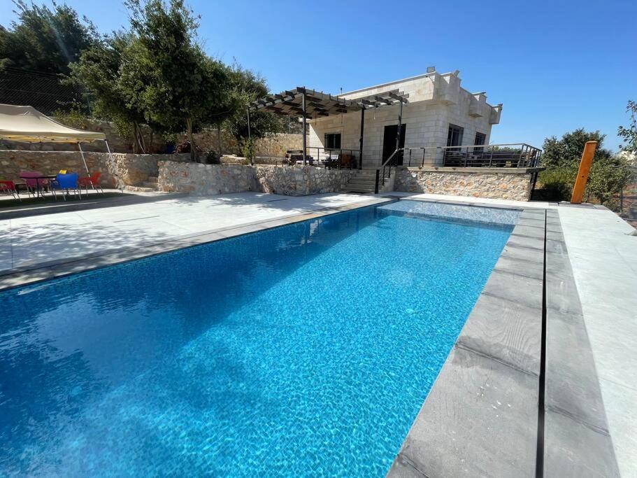 a swimming pool with blue water in front of a house at Oak Farm مزرعة البلوط in Ajloun