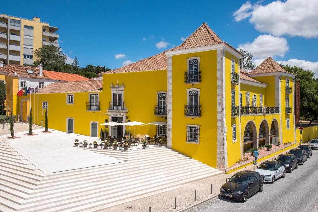 un bâtiment jaune avec des voitures garées devant lui dans l'établissement Vila Gale Collection Palácio dos Arcos, à Oeiras