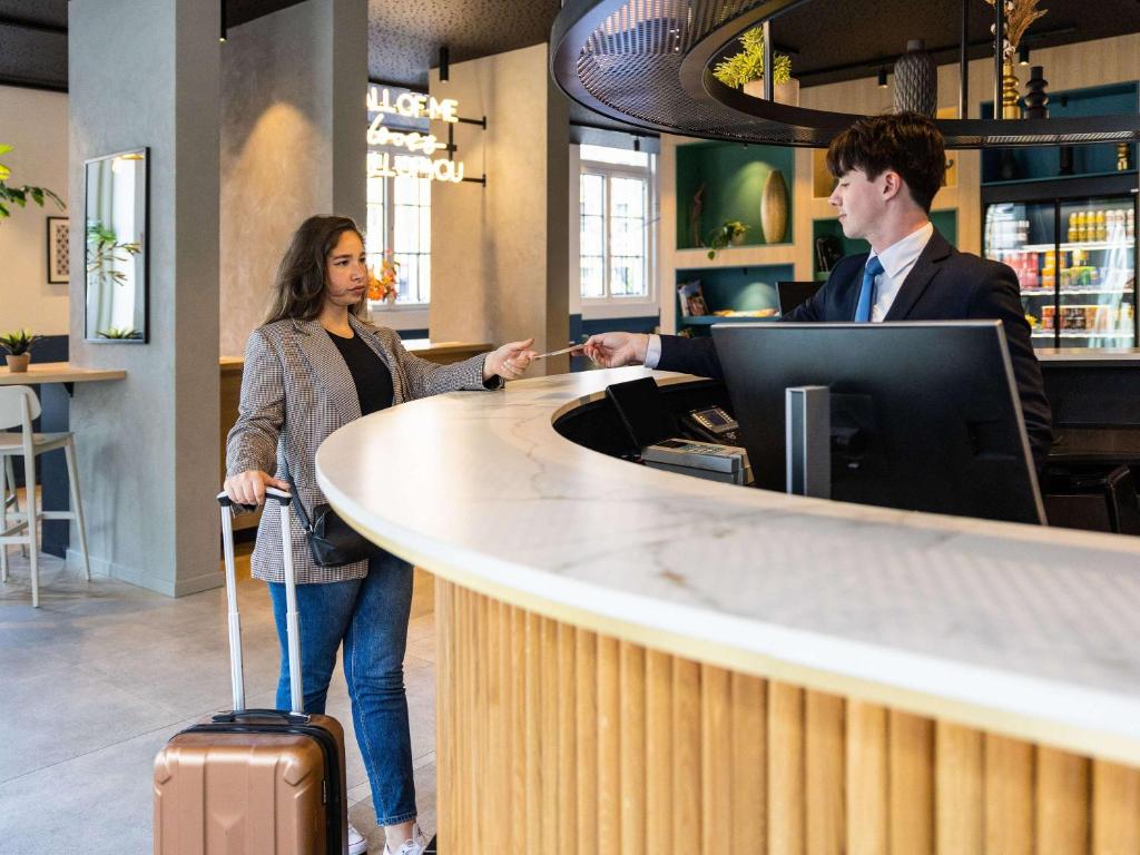 a man and a woman with a suitcase standing at a counter at Hotel Novotel Brussels Off Grand Place in Brussels