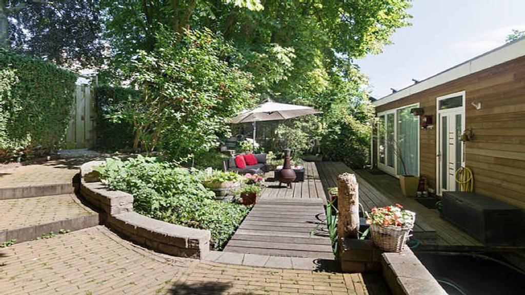 un patio trasero con una terraza de madera con sombrilla en Studio in Woonboot + privébadkamer en -tuinterras, en Utrecht