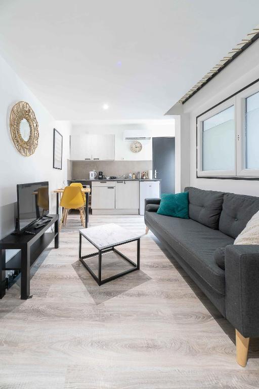 a living room with a gray couch and a kitchen at Résidence Le Celest - Appartements climatisés - Centre ville in Vichy