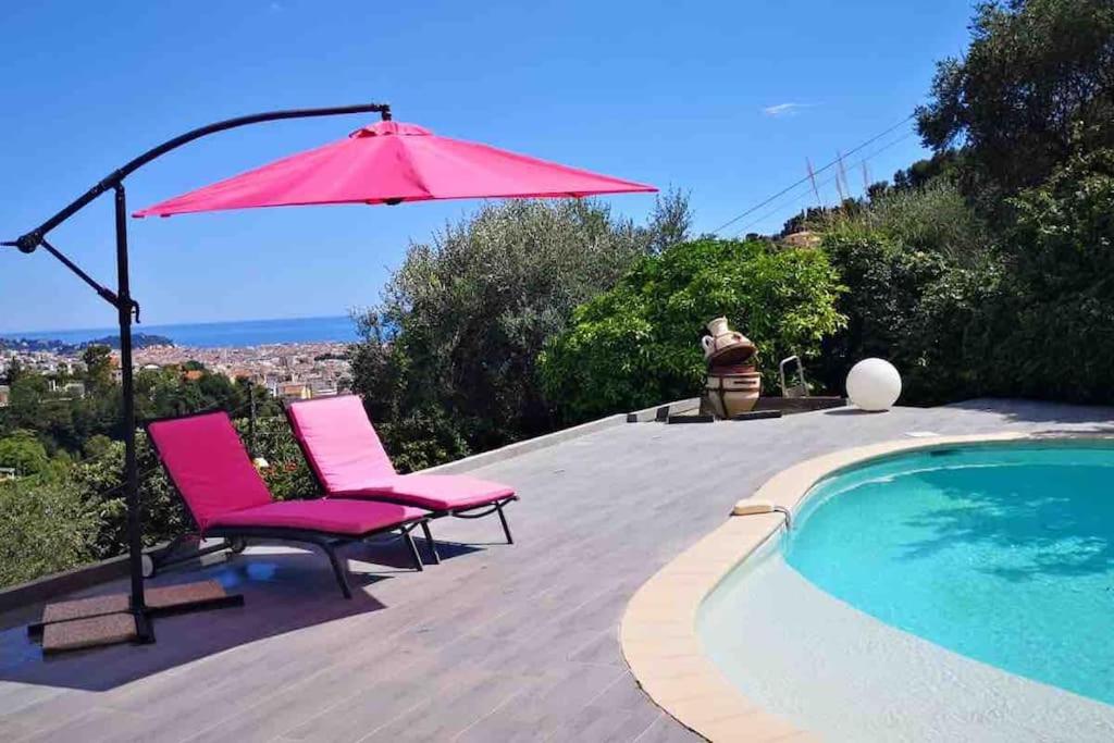 une paire de chaises roses et un parasol à côté d'une piscine dans l'établissement Villa avec piscine et vue magnifique sur Nice, à Nice