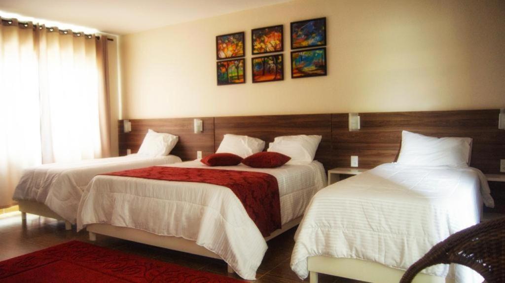 a bedroom with two beds with white sheets and red pillows at POUSADA DELVILLE in Itapoa