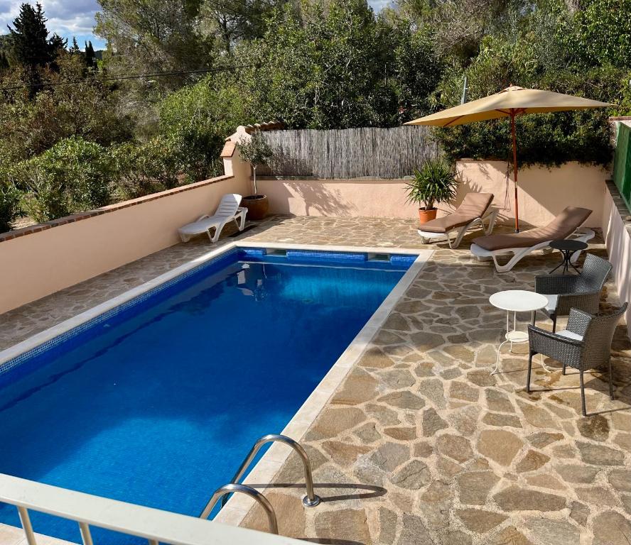 a swimming pool with chairs and an umbrella next to it at Apartment in country house with views and pool in Vespellá