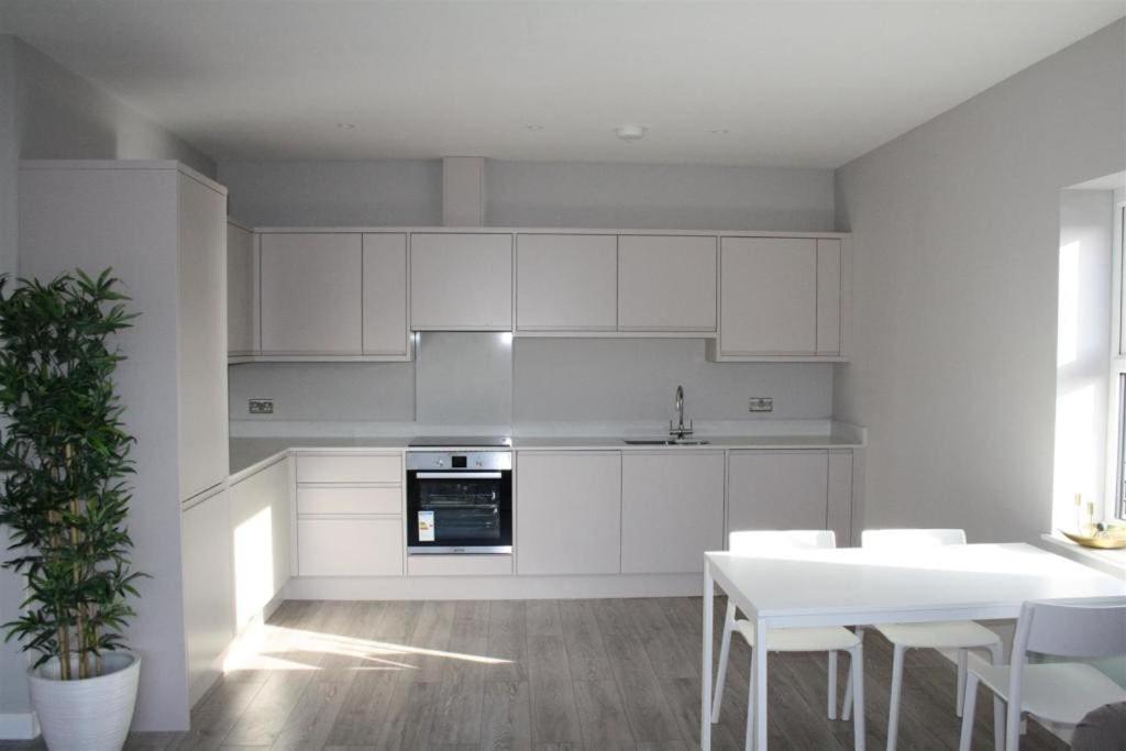 a kitchen with white cabinets and a table and chairs at Superb New Build 2 Bed Flat - 6 Ophelia Court in Epsom