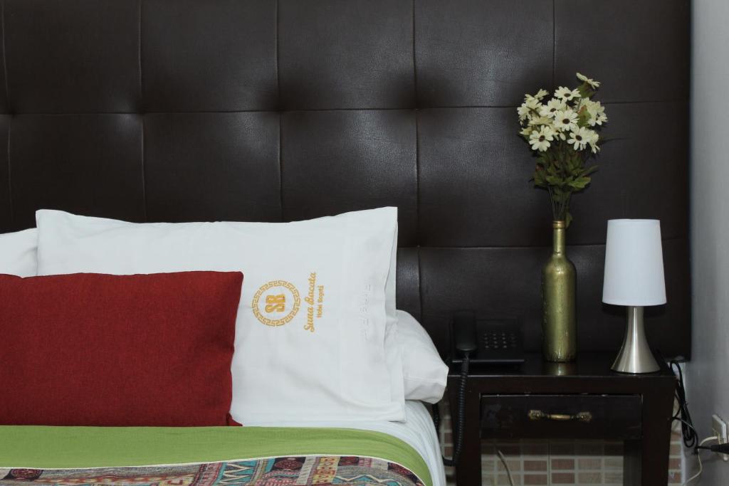 a bed with a red pillow and a vase of flowers on a table at Suna Bacata in Bogotá