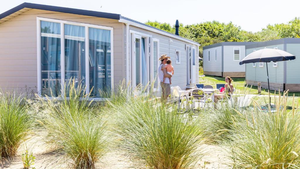 una pareja de pie frente a una casa en Molecaten Park Noordduinen en Katwijk aan Zee