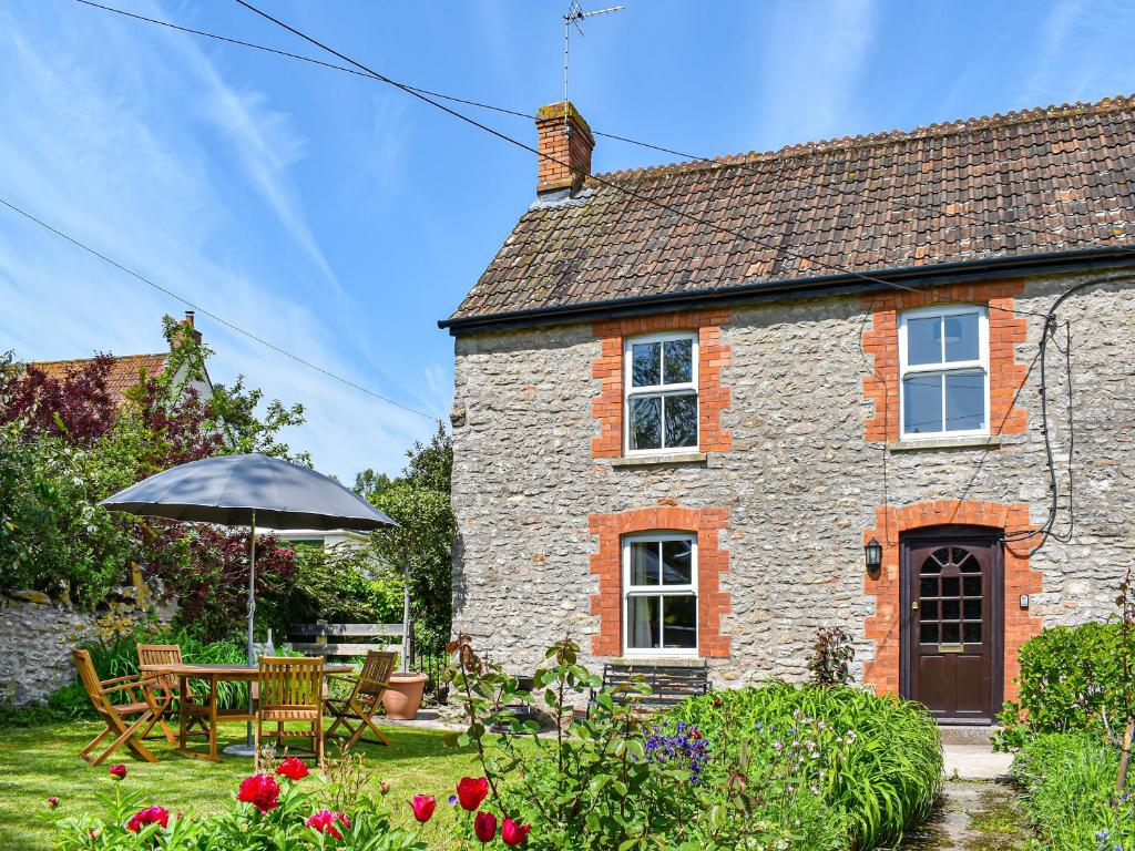 a stone house with a table and an umbrella at Poplar Farm Cottage in Westbury-sub-Mendip