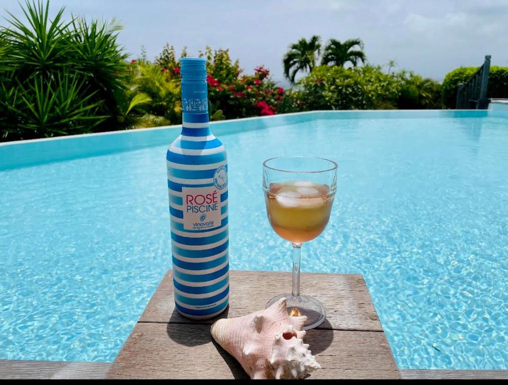 a bottle of wine and a glass next to a swimming pool at Villa Libellule in Grand-Bourg