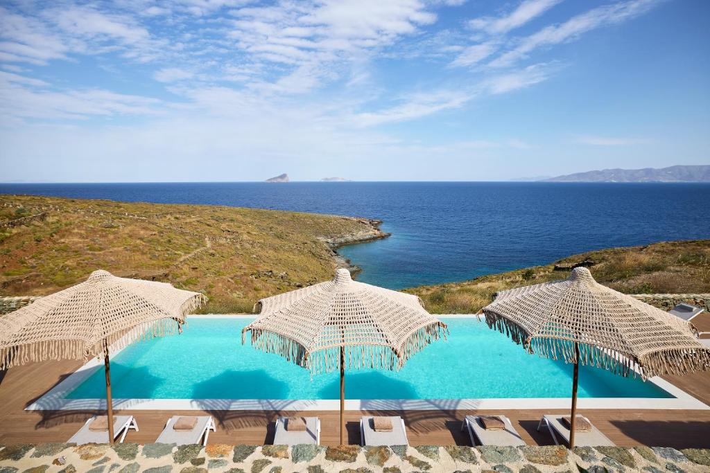 una piscina con sombrillas y sillas y el océano en Ianemi Suites by K4 Kythnos, en Kithnos