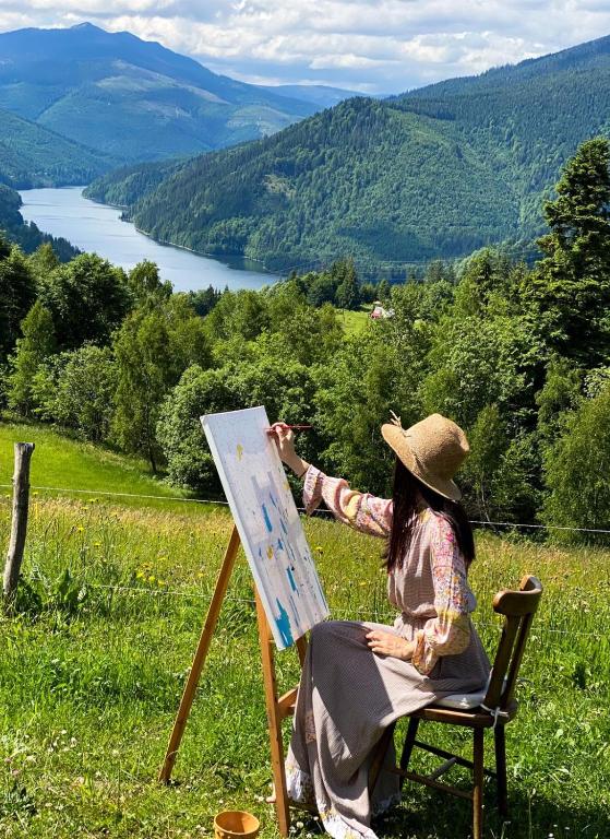 a woman sitting in a chair painting a canvas at Casa Maria Valea Draganului in Lunca Vişagului