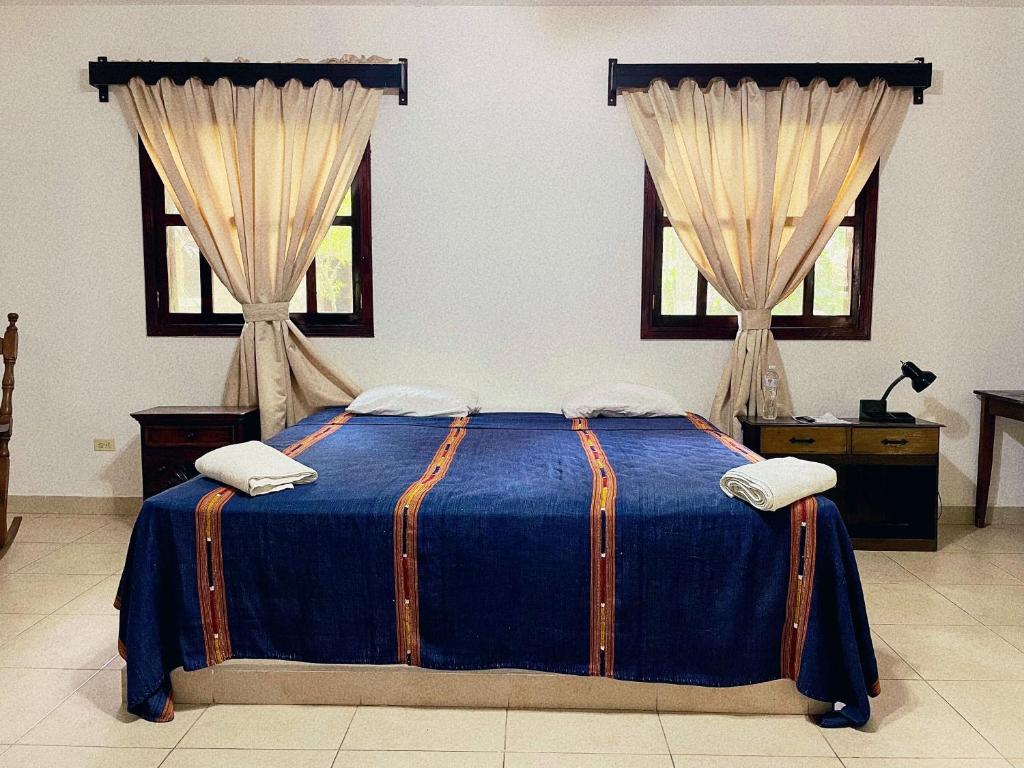 um quarto com uma cama azul e 2 janelas em El Bosque Hotel em Copán